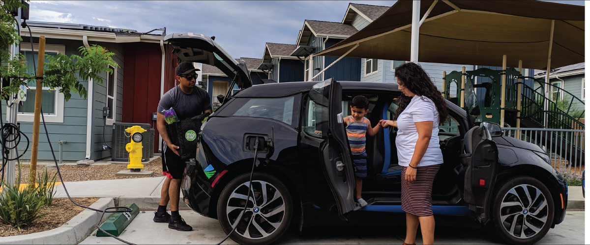 Family unloading groceries from a zero-emission vehicle plugged into a charger in front of a home